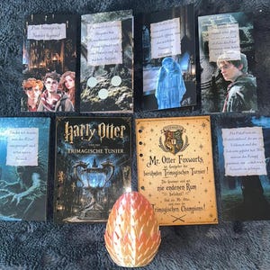 Könnte beinhalten: Eine Sammlung von sieben rechteckigen Karten mit Harry-Potter-Motiven und deutschem Text sowie einem zentralen, dreidimensionalen, schuppenartig texturierten, orange-gelben eiförmigen Objekt. Die Karten zeigen verschiedene Szenen und Figuren.