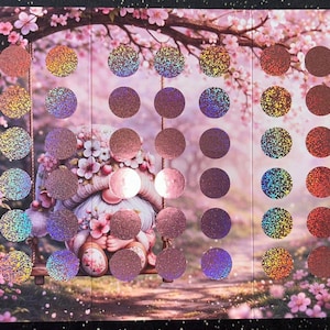 Könnte beinhalten: Eine dekorative Palette mit einer skurrilen Gartenszene mit einem Zwerg auf einer Schaukel, umgeben von rosa Blüten. Die Palette enthält eine Vielzahl runder Lidschatten in schimmernden und matten Ausführungen, mit Farben von Rosa bis Braun.