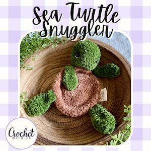 May include: A plush sea turtle snuggler toy with a dark green head and flippers and a textured brown circular body. The toy features black safety eyes and a small white fabric tag on the side that reads Crochet with JB. The text Sea Turtle Snuggler is displayed in black script above the toy.