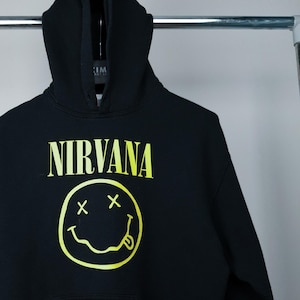 May include: Black hoodie with a yellow smiley face and the word "NIRVANA" printed on the front.