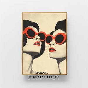Puede incluir: Dos mujeres con cabello negro que llevan gafas de sol ovaladas rojas. Las mujeres miran hacia arriba y sus caras están juntas. El fondo es de color beige claro.