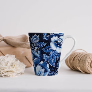 May include: A white-handled mug with a dark blue floral pattern. The design features white flowers and leaves against a navy background. A roll of twine and a wrapped gift are in the background.
