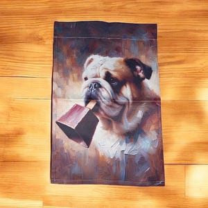 Garden flag featuring a painted portrait of a bulldog holding a maroon cowbell in its mouth, with a warm, abstract background that creates a charming and whimsical atmosphere.