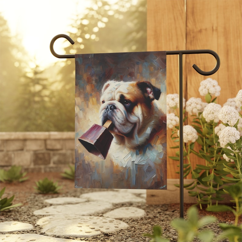 Garden flag featuring a painted portrait of a bulldog holding a maroon cowbell in its mouth, with a warm, abstract background that creates a charming and whimsical atmosphere.