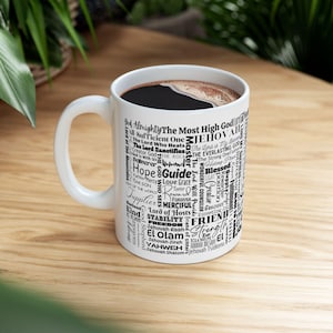 May include: White ceramic mug with a black design of words and phrases related to God and faith. The words are arranged in a circular pattern and include "God Almighty", "Jehovah", "Hope", "Guide", "Friend", "Strength", and "Lord of Hosts".