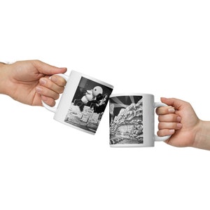 May include: Two white ceramic mugs with black and white illustrations. One mug features a cartoon astronaut delivering pizza on the moon. The other mug shows a scene of a lunar landscape with a building in the distance.