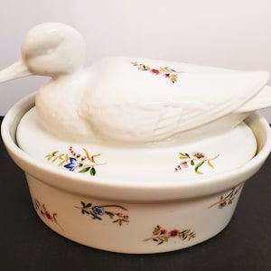 May include: White ceramic duck-shaped serving dish with a floral design. The lid is shaped like a duck and has a floral design.