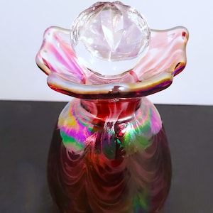 May include: A vintage iridescent glass bottle with a clear glass stopper. The bottle has a pink, green, and purple swirl pattern.