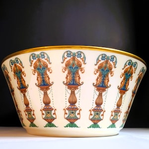 May include: A large, white ceramic bowl with a gold rim and intricate blue, green, and brown floral designs. The bowl is perfect for serving salads, fruit, or other dishes.