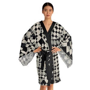 Può includere: Accappatoio kimono a fantasia bianca e nera con scollo a V e cintura nera. L'accappatoio presenta un design geometrico di forme bianche e nere. Le maniche sono ampie e fluide e l'accappatoio arriva al ginocchio.