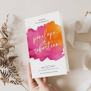 May include: A wedding invitation with a watercolor design in shades of pink and orange. The names "penelope + sebastian" are written in elegant script. The date and venue are also displayed.