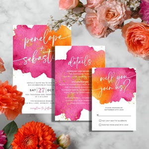May include: Wedding invitation suite with watercolor design. The set includes an invitation, details card, and RSVP card. The cards feature pink and orange watercolor backgrounds with gold accents and elegant script. Floral arrangement in the background.