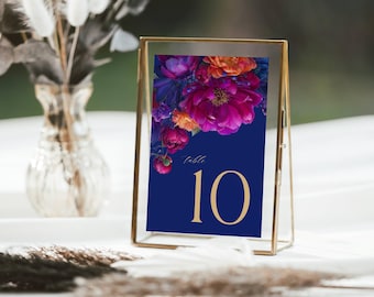May include: A table number card in a gold frame. The card has a navy blue background with a floral design in shades of pink, purple, and orange. The number "10" is displayed in gold. The word "table" is written in white.