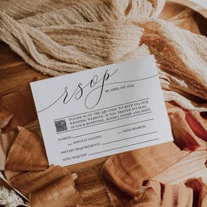May include: A white RSVP card with a black script font RSVP and a QR code. The text reads "Please scan the QR code to RSVP via our wedding website. If you prefer to mail in your response, kindly stamp and post." The card has lines for names, joyfully accepts, dietary requirements, song request, and sadly regrets.