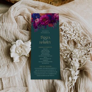 May include: A wedding order of service card with a dark teal background and floral design. The card features the names "Tania & Harry" in gold lettering, the order of service, and a thank you message. White flowers and fabric surround the card.