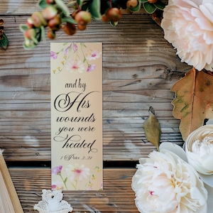 May include: A beige bookmark with floral designs and the text "and by His wounds you were healed 1 Peter 2:24".