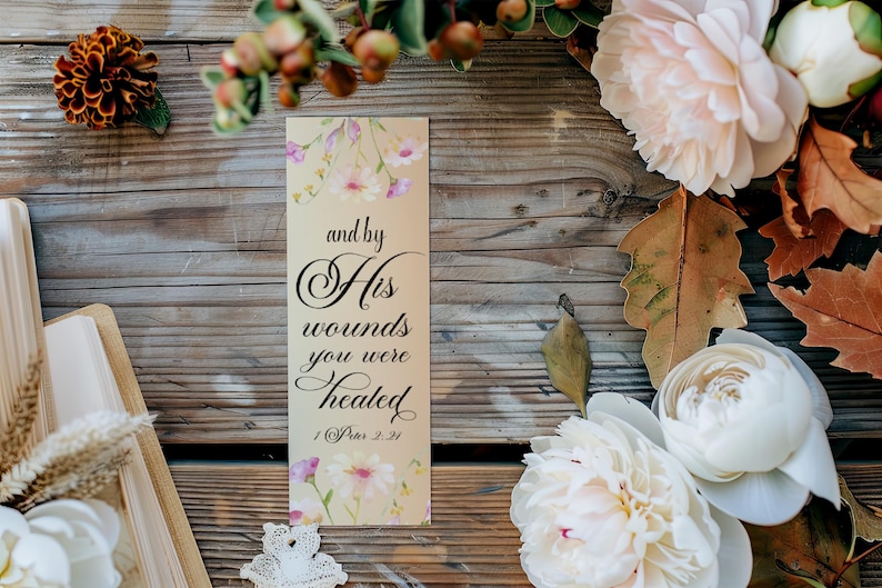 May include: A beige bookmark with floral designs and the text "and by His wounds you were healed 1 Peter 2:24".