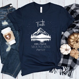 Könnte beinhalten: Marineblaues T-Shirt mit einer weißen Grafik einer Bergkette und einem Kreuz. Der Text "Faith can move mountains Mark 11:23" ist unter der Grafik gedruckt.