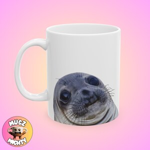 Op de afbeelding: Witte keramische mok met een close-up afbeelding van een zeehond met een verraste uitdrukking. De ogen van de zeehond zijn wijd open en zijn mond staat lichtjes open.