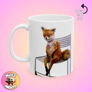 May include: White ceramic mug with a fox sitting on a metal chair. The fox has a sad expression and is looking down. The mug has a white background and the image is centered.
