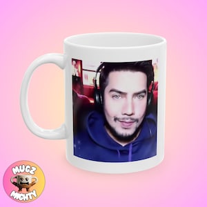 May include: White ceramic mug with a color image of a man wearing headphones and a blue hoodie. The man is looking at the camera and smiling.