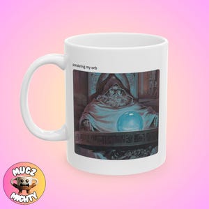 May include: White ceramic mug with an illustration of a wizard contemplating a blue orb. The text "pondering my orb" is above the image. The mug has a curved handle and a cartoon mug logo.