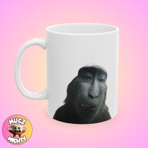 May include: White ceramic coffee mug with a black and white image of a monkey's face on the front.
