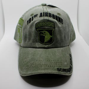 Puede incluir: Una gorra de béisbol verde con el texto "101st AIRBORNE" y un parche de águila. La gorra también tiene las palabras "SCREAMING EAGLES" bordadas en el lateral. El sombrero está hecho de una tela verde descolorida.
