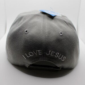 May include: A gray baseball cap with the embroidered text "I LOVE JESUS" in white. The cap has a curved brim and a small tag attached to the top.