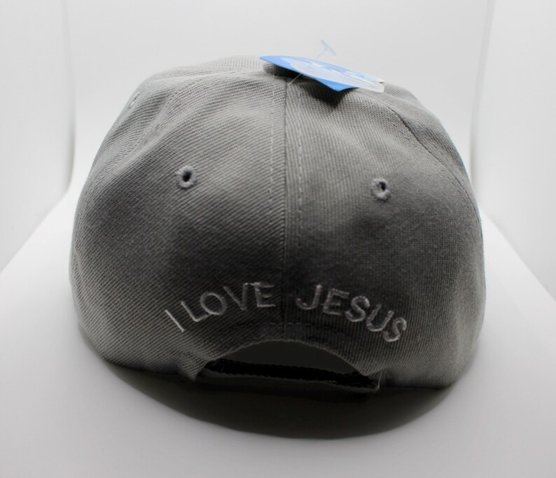 May include: A gray baseball cap with the embroidered text "I LOVE JESUS" in white. The cap has a curved brim and a small tag attached to the top.