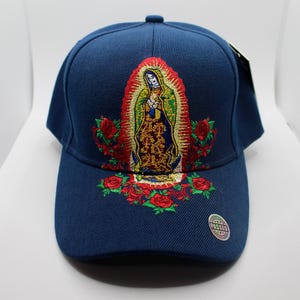 May include: A dark blue baseball cap with an embroidered image of the Virgin Mary surrounded by red roses. The cap has a curved brim and a white tag with the word "PASSED" on it.