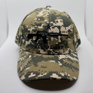 Op de afbeelding: Een camouflage baseballpet met een digitaal camopatroon in groen, bruin en beige tinten. De pet heeft een zwarte afbeelding van een geweer en de tekst "COME AND TAKE IT" geborduurd op de voorkant.