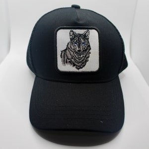May include: Black trucker hat with a white patch featuring a wolf with blue eyes.