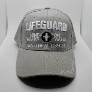 May include: Gray baseball cap with the word "LIFEGUARD" embroidered in white. The cap also features the text "MINE WALKS ON WATER" and "MATTHEW 14:25-33". The brim has the words "I LOVE JESUS" embroidered in white.