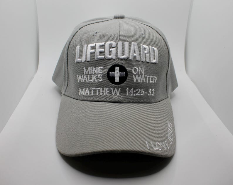 May include: Gray baseball cap with the word "LIFEGUARD" embroidered in white. The cap also features the text "MINE WALKS ON WATER" and "MATTHEW 14:25-33". The brim has the words "I LOVE JESUS" embroidered in white.