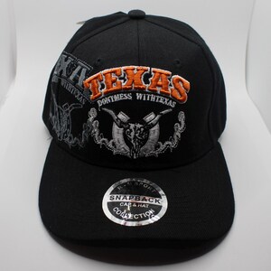 Puede incluir: Gorra snapback negra con "TEXAS" bordado en naranja y blanco, y un diseño de calavera de cuernos largos. La gorra también presenta el texto "DON'T MESS WITH TEXAS" y una pegatina "Snapback Cap & Hat Collection".