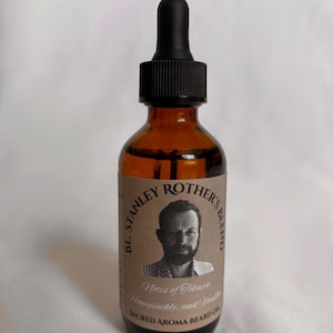 Puede incluir: Una botella de vidrio marrón con un gotero negro y una etiqueta que dice "B.L. Stanley Rother's Blend" con la cara de un hombre. La etiqueta también dice "Notas de tabaco, madreselva y vainilla" y "Aceite de barba Sacred Aroma".