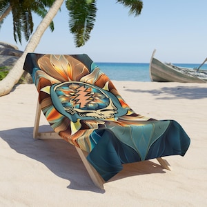 May include: A beach towel draped over a wooden beach chair. The towel features a colorful, psychedelic design with a skull and lightning bolt motif. The background shows a sandy beach, palm trees, and a boat.