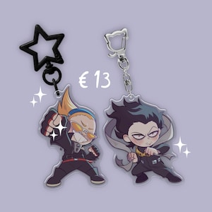 May include: Two anime-style keyrings featuring characters in action poses. One keyring has a black star-shaped clasp, the other a silver clasp. The characters are wearing black outfits. The price is €13.