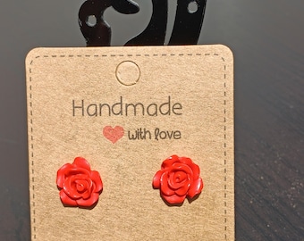 May include: A pair of red rose stud earrings on a brown card with the text "Handmade with love".