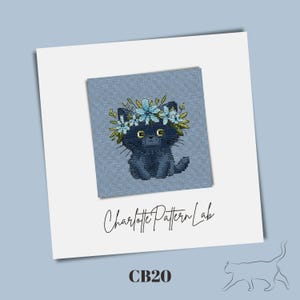 May include: A cross-stitch design of a black cat wearing a floral crown, set against a blue fabric background. The design is on a square, with the text "Charlotte Pattern Lab" and "CB20" below. The cat has yellow eyes.