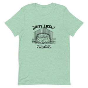 Peut inclure: Un t-shirt vert avec un graphique noir d'une meule de foin et le texte "MOST LIKELY TO FALL ASLEEP IN THE HAYSTACK".