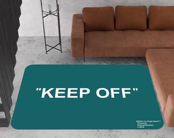May include: A teal blue rug with the text "KEEP OFF" in white letters. The rug has a small white text label in the bottom right corner that reads "IKEA © by Virgil Abloh™ "Flooring" Älmhult, Sweden © 2018."