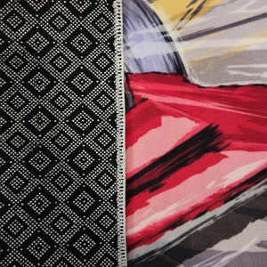 May include: Close-up of a black and white patterned rug with a white border. The rug is next to a red, white, and gray abstract design.