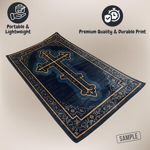 May include: A rectangular navy blue rug featuring a large cross design in a lighter shade of blue, outlined with gold-colored filigree. The border of the rug also has a gold floral pattern. The rug is labeled "Portable & Lightweight" and "Premium Quality & Durable Print".
