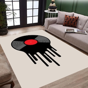 May include: A white rug with a black vinyl record design. The record is dripping black paint. The record has a red center label.