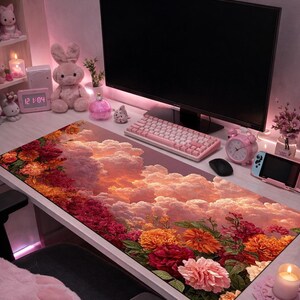 May include: A floral mouse pad featuring a vibrant design of flowers and clouds in shades of red, orange, and pink. The desk setup includes a pink keyboard, monitor, and other accessories, creating a cohesive aesthetic.