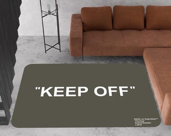 May include: A dark gray rug with the text "KEEP OFF" in white letters. The rug has a small white text label in the bottom right corner that reads "IKEA c/o Virgil Abloh* "Flooring"  Almhult, Sweden © 2019"