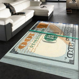 May include: A rug featuring a stack of $100 bills with a green rubber band around them. The bills are arranged in a way that the top bill is folded over the rest of the stack. The rug is light blue and has a white background.