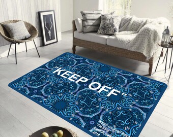 May include: A blue and white patterned rug with the text "KEEP OFF" in white lettering. The rug has a floral design with intricate details. The text "IKEA® c/o Virgil Abloh™" is printed in the bottom right corner of the rug.